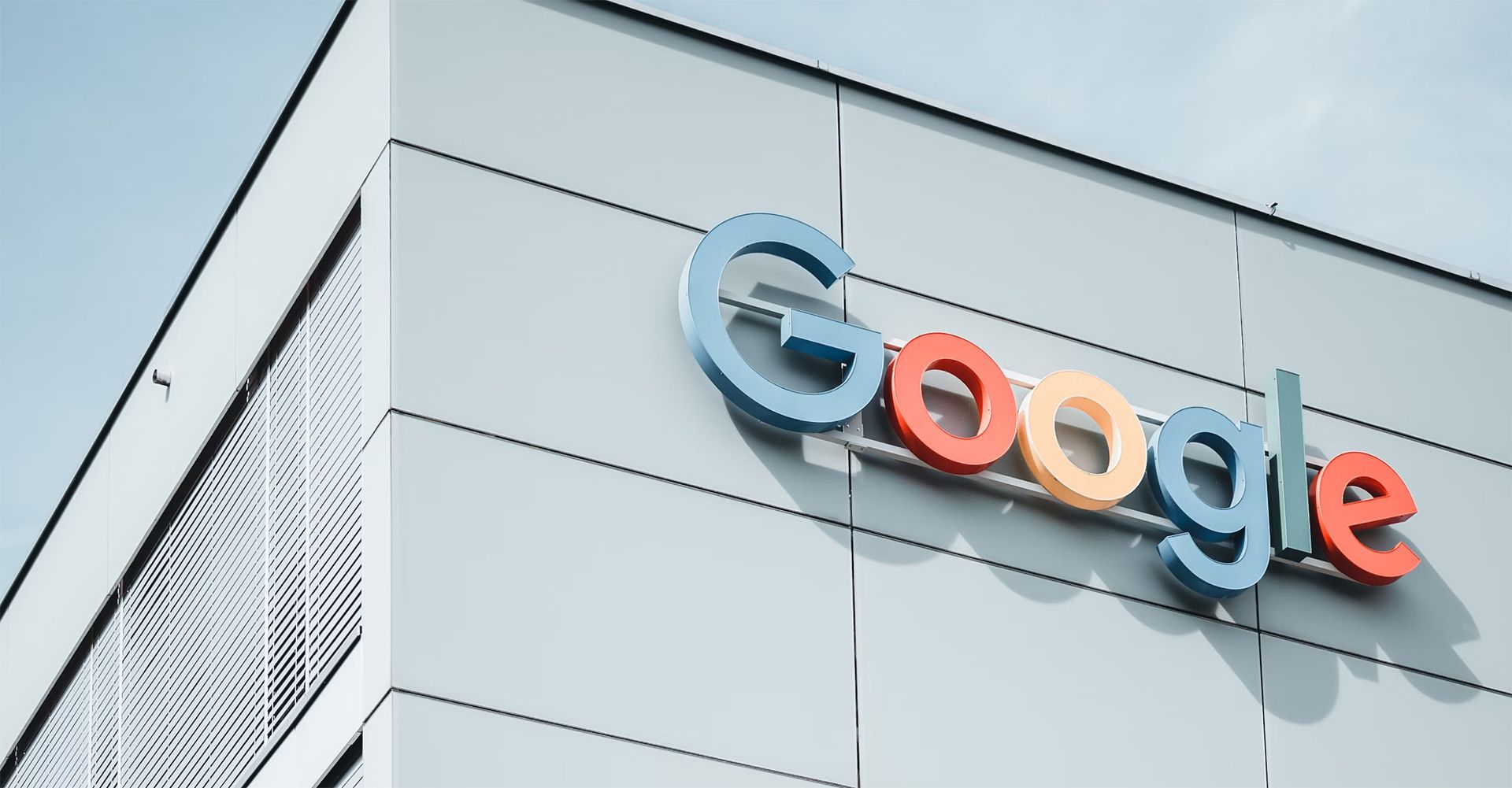 Google-Logo an der Fassade eines modernen Bürogebäudes unter blauem Himmel.