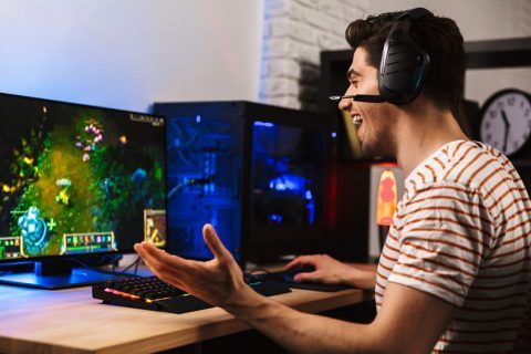 Lächelnder Gamer mit Headset spielt Strategiespiel am Computer in einem beleuchteten Zimmer.